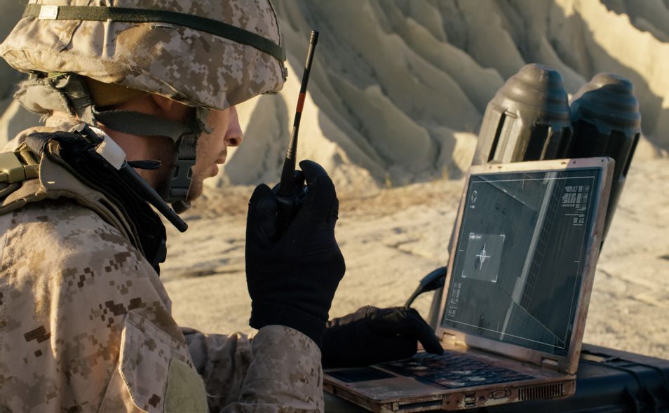 A soldier working on a rugged laptop in the desert